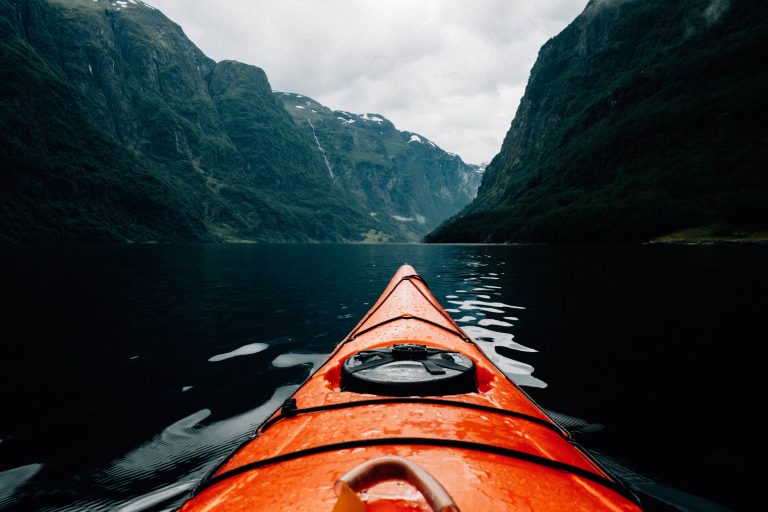 Paseo en kayak hinchable naranja en un fiordo rodeado de montañas