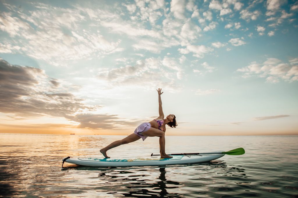 Chica practicando yoga sobre tabla de paddle surf