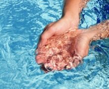 manos tocando agua limpia de una piscina
